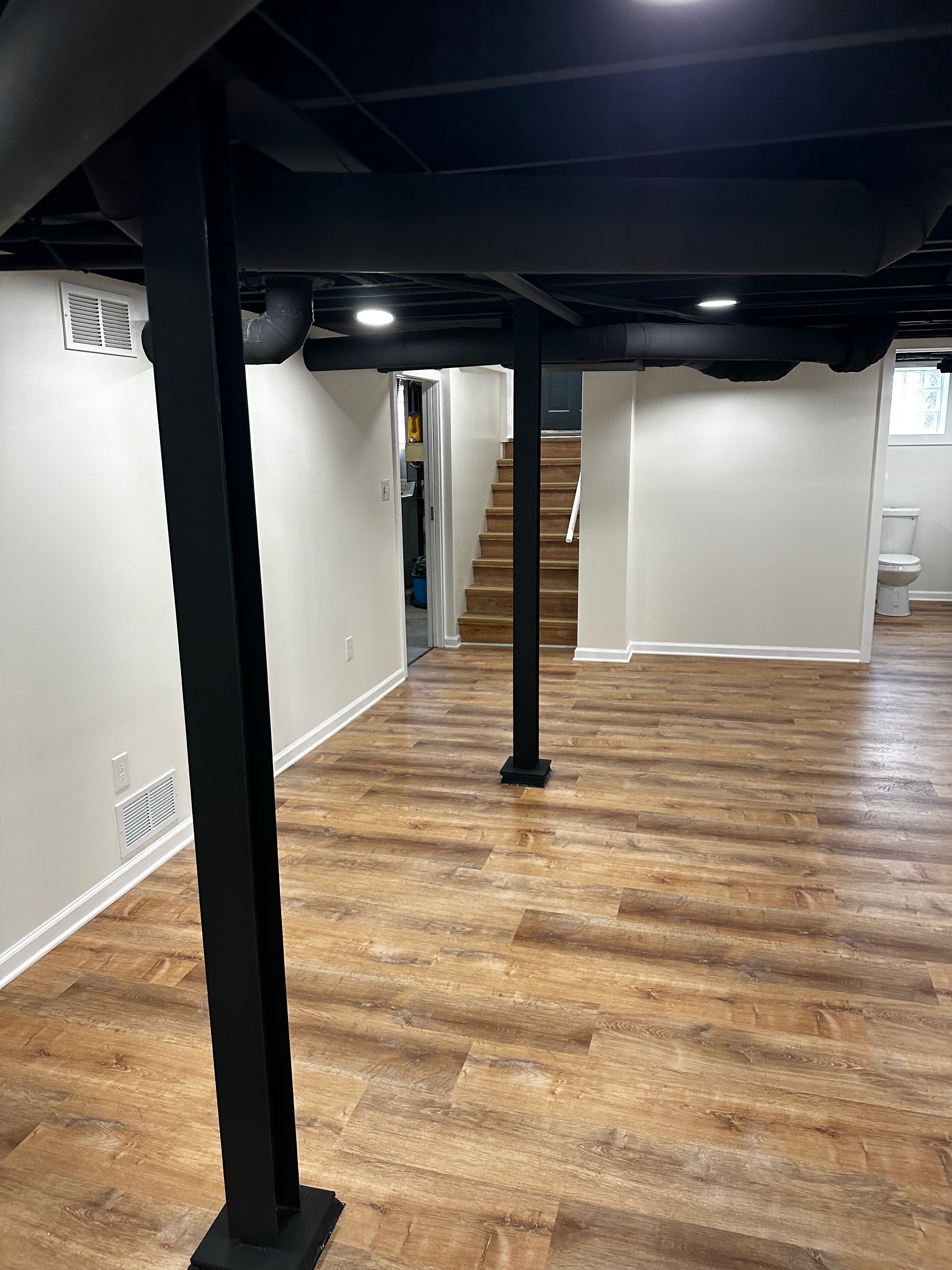 Finished open basement gym area with wood-look flooring and painted open ceiling