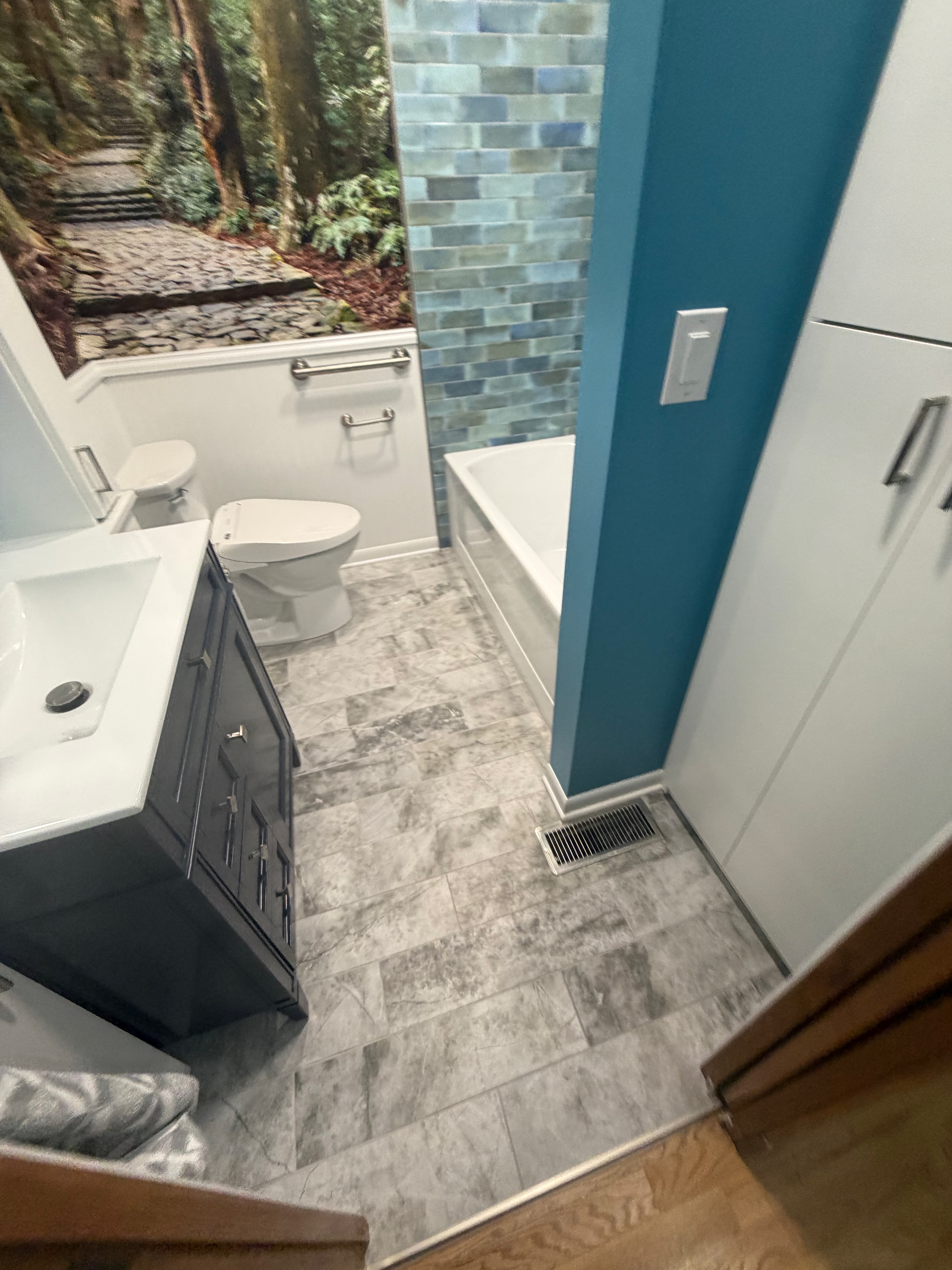 Finished bathroom with blue-green tile, mural, vanity and patterned floor